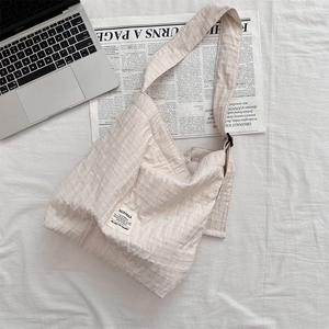 Detail of beige pleated canvas bag with wide strap and brand label on white fabric