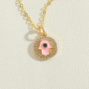 Close-up of golden necklace with pink Hamsa Hand pendant and white zircon inlay