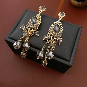 Detailed shot of retro gold teardrop earrings with grey crystals on black leather display