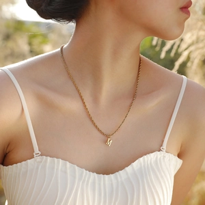 Detail of a minimalist gold twisted chain necklace with a capital M letter pendant