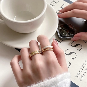 Stacked golden wave ring and white enamel band shown on hand with modern lifestyle accessories