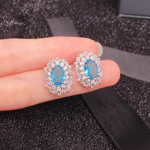 Silver stud earrings with oval blue gemstone and zircon halo on black texture
