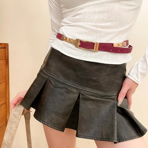 Detail of burgundy leather belt with gold buckle styled on a black pleated skirt