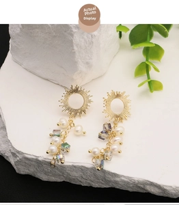 Detail of 18k gold plated sunburst earrings with natural pearls on white stone