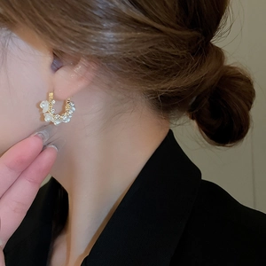 Macro detail of gold C-shaped earrings with white floral petals and faux pearls for women