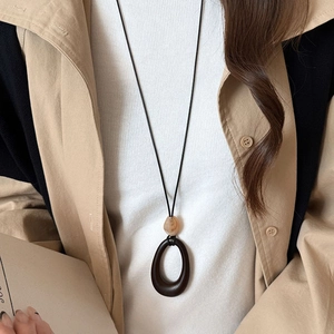 Detail of vintage acrylic pendant necklace showing amber bead on beige trench coat