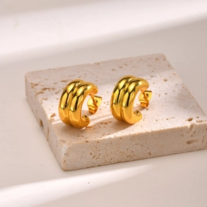 Detail of two-tone gold double layer C-shaped earrings on a beige stone base