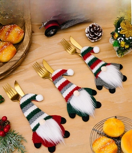 Three Christmas gnome cutlery holders with striped hats set on a festive wooden table