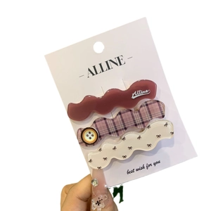 Three-piece set of wave-shaped hair clips in red plaid and solid colors on a display card
