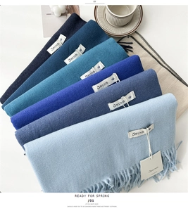 Detail of stacked cashmere-feel scarves in blue shades with tassels and brand labels