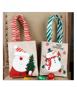 Detail of burlap Christmas gift bags with Santa and Snowman embroidery on a rustic chair