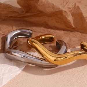 Detail of irregular liquid wave bangles in gold and silver with mirror polish finish
