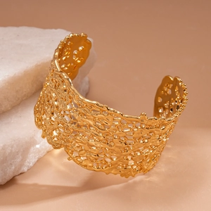 Close-up of golden irregular hollow textured cuff bracelet on decorative stone background