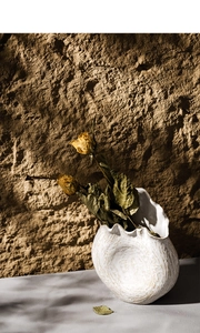 Close-up of a white shell-shaped ceramic vase with textures and dried yellow roses