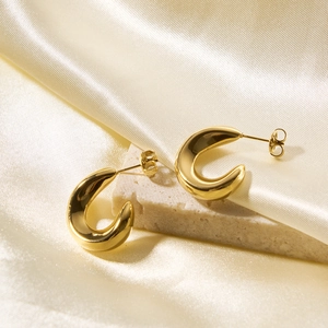 Detailed close-up of golden hollow C-shaped earrings on beige stone and silk fabric