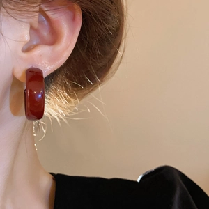 Close-up of a model wearing a glossy deep red resin hoop earring with retro design