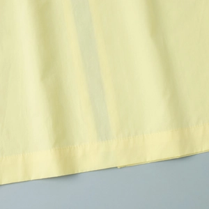 Macro view of light yellow cotton fabric hem showing precise stitching and smooth texture