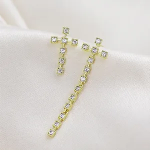 Detalle de pendientes de cruz asimétricos dorados con pavé de circonitas claras