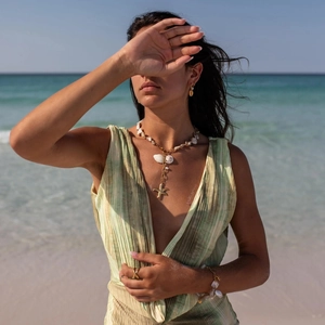 Detail of a gold starfish pendant necklace with natural shells on a beach background
