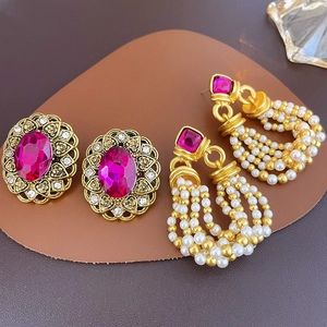 Close-up of vintage court style earrings with magenta crystals and pearl tassels on a leather tray