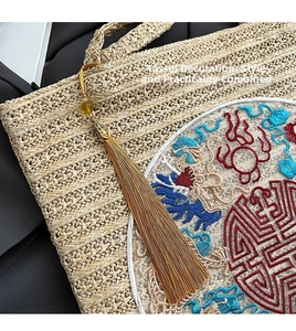 Close-up of woven straw tote bag with intricate Chinese dragon embroidery and long tassels