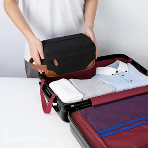 Large men's canvas and leather toiletry bag being placed into a suitcase