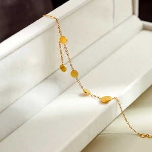 Detail of a minimalist gold bracelet with round charms on a white velvet jewelry box
