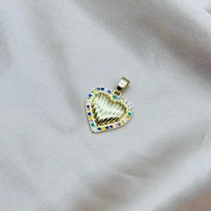 Dettaglio macro del ciondolo a cuore dorato con zirconi colorati e trama a raggi