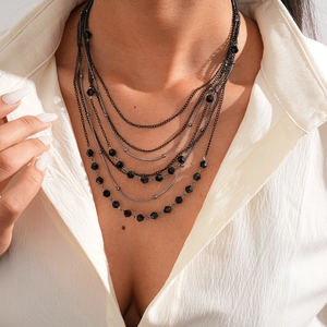 Detail showing multi-layered black beaded necklace styling on a white shirt neckline