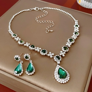 Detailed view of silver jewelry set with emerald drop stones and sparkling crystals