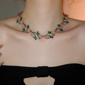 Detail of vintage necklace with pink resin stone and green leaf accents on model