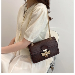 Detail of a brown faux-crocodile leather bag featuring a gold rhinestone bee clasp