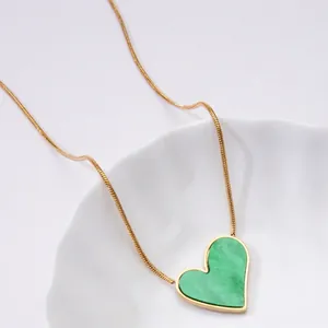 Detail of heart pendant necklace with green stone inlay on elegant gold snake chain