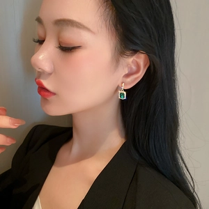 Close-up of green emerald-cut earring with gold metal and diamond accents on a model
