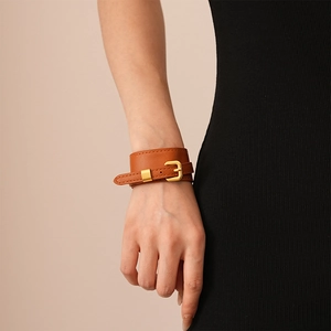 Detail of a brown leather wide cuff bracelet with a golden buckle on a model's wrist