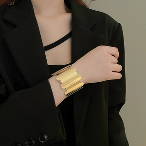 Detail of a wide gold cuff bracelet featuring a unique wavy textured metal surface