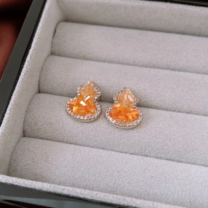 Close-up of gold gourd earrings with orange faceted gemstone and micro-pave setting