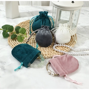 Velvet drawstring jewelry pouches in various colors displayed on a woven mat