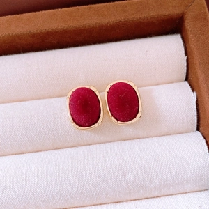 Macro shot of oval red velvet stud earrings with gold metallic borders on a display stand