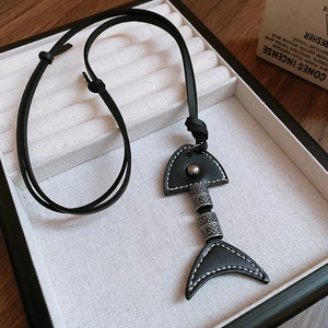 Detail of fishbone pendant necklace with leather accents and engraved metal beads