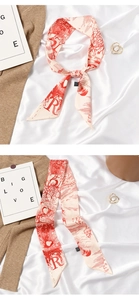 Detail view of beige silk twilly scarf with red letter R pattern and elegant ribbon bow