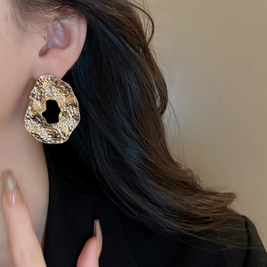 Macro shot of gold geometric earrings with hammered texture and irregular hollow design