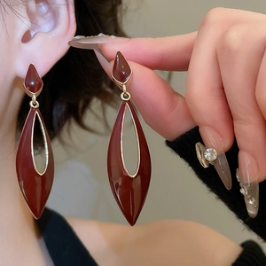 Detail view of hollow water drop earrings with dark red enamel and golden alloy frames