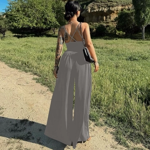Detail of grey backless jumpsuit showing criss-cross straps and wide-leg design outdoors