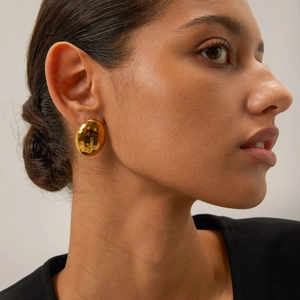 Detailed view of hammered 18k gold oval earrings worn by a model in a minimalist style