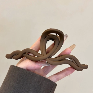 Gros plan d'une pince à cheveux mate marron foncé avec design ondulé tenue à la main