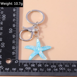 Detail of light blue starfish keychain with glitter finish weighing 10.7g on scale ruler