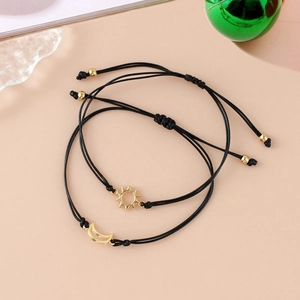Detail of adjustable black woven bracelets with gold sun and moon pendants on pink background