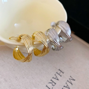 Detail of twisted multi-layer hoop earrings in gold and silver on a white ceramic cup