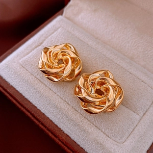 Macro shot of gold-toned floral stud earrings with intricate spiral texture on beige velvet